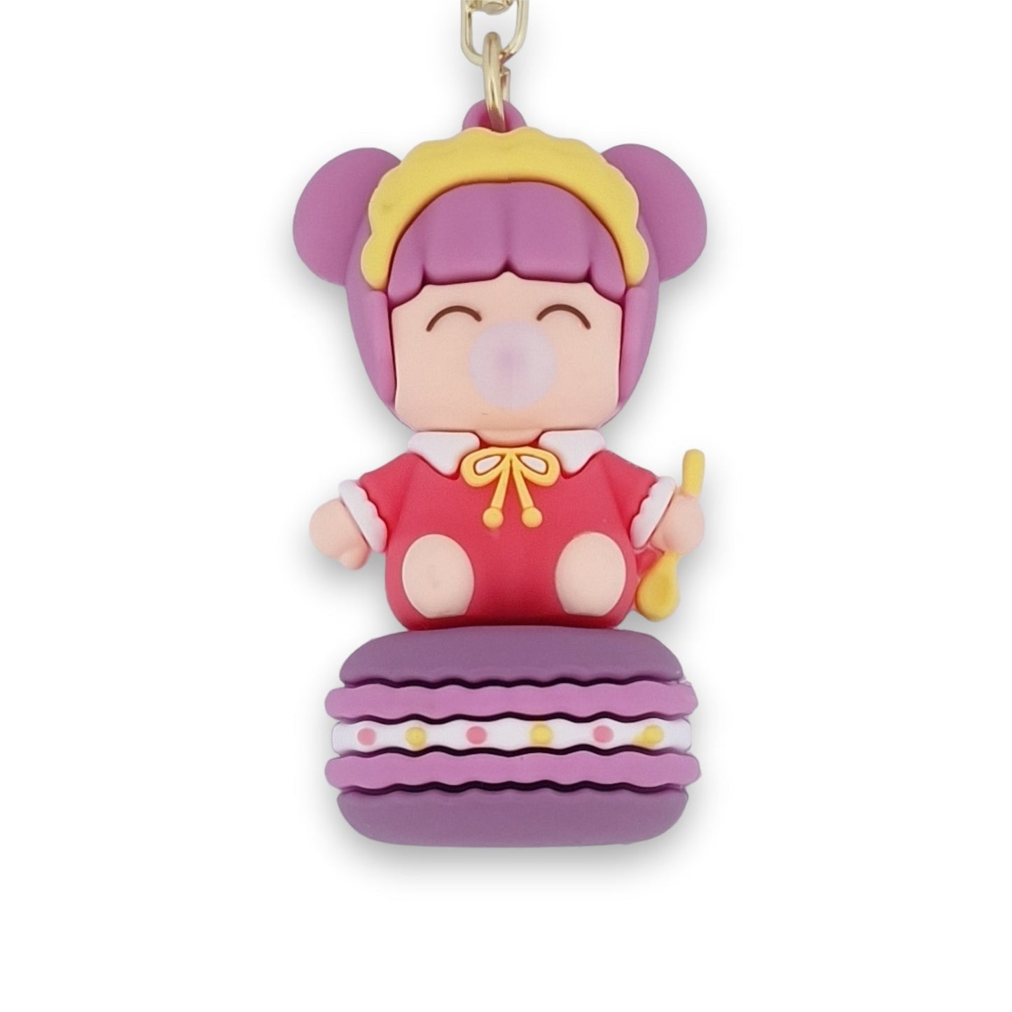 Niedlicher Baby-Schlüsselanhänger auf lila Macaron, mit rosa Haaren, rotem Outfit und gelbem Löffel, bläst Kaugummiblase