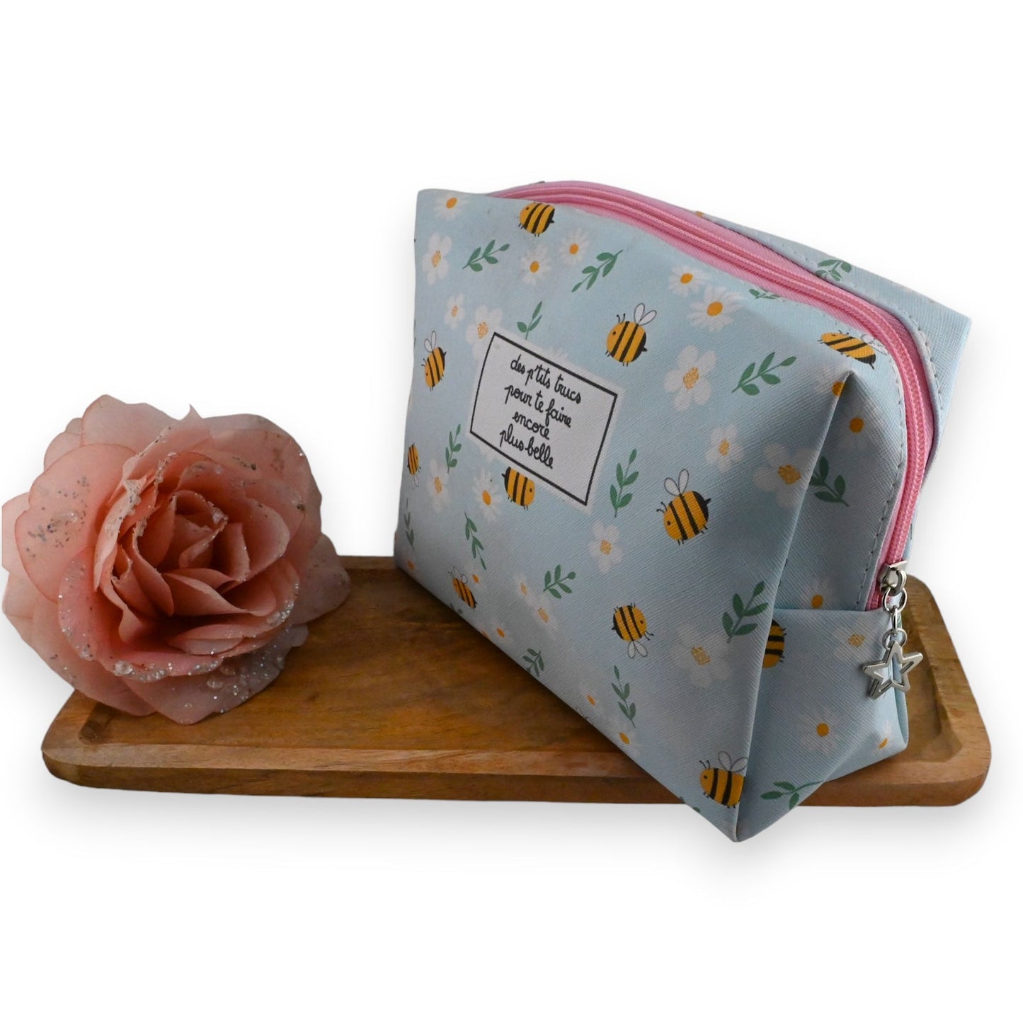 Toilettentasche mit Bienenmuster, rosa Reißverschluss und Sternanhänger neben rosa Rose auf Holzbrett