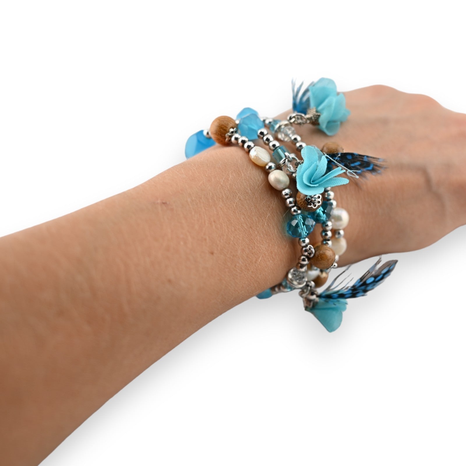 Elastische Modeschmuckarmbänder mit türkisfarbenen Blüten, Federn, Perlen und Kristallen am Handgelenk einer Frau