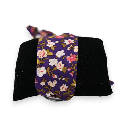 Elegante Armbanduhr mit violettem Blumenmuster-Stoffarmband auf schwarzem Samtkissen, florales Design