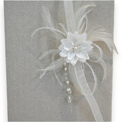 Eleganter weißer Haarschmuck mit Blüte, Federn und Perlen auf glitzerndem Hintergrund, perfekt für Bräute